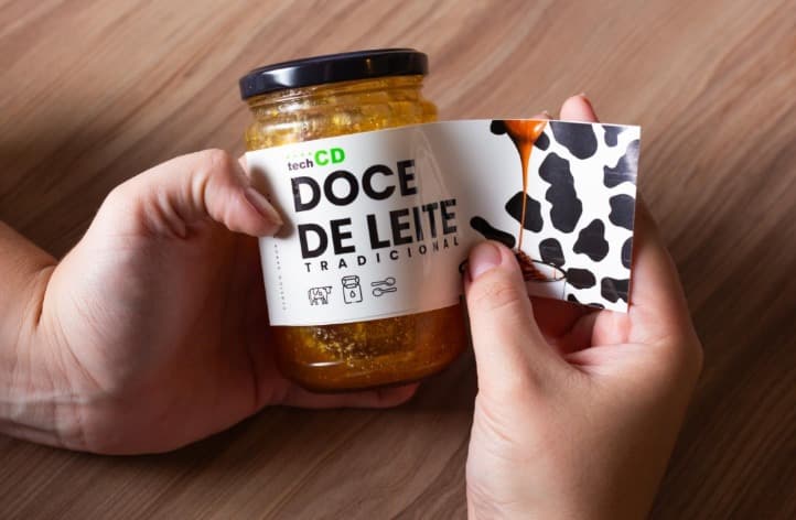 Mãos aplicando rótulo personalizado de doce de leite em pote de vidro